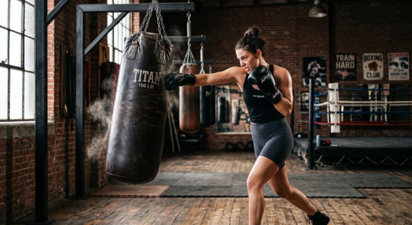 A female boxer hitting a heavy bag with proper stance and boxing gloves during training in a gym.